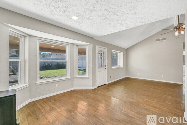 A spacious room with wooden flooring and large windows.