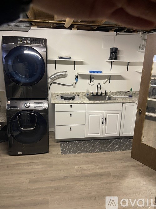 A black front load washing machine is in a laundry room with a white sink and cabinets.