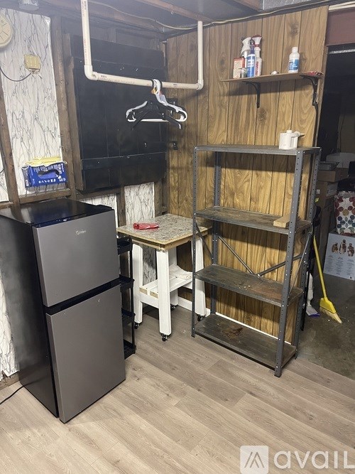 A black refrigerator is in a room with a wooden shelf and a white table.