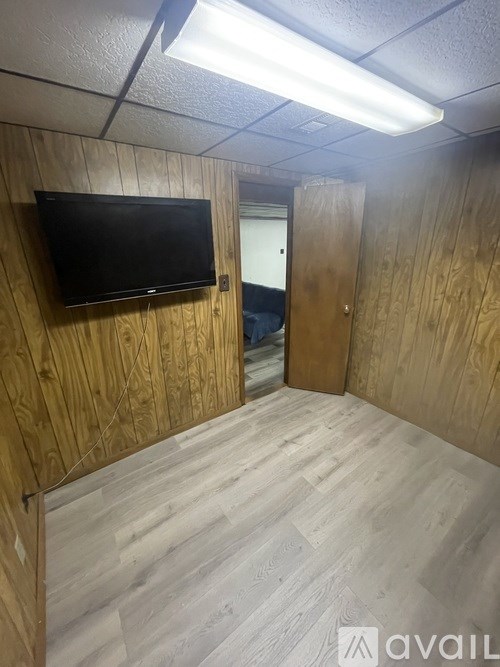 A room with a television on the wall and a doorway leading to another room.