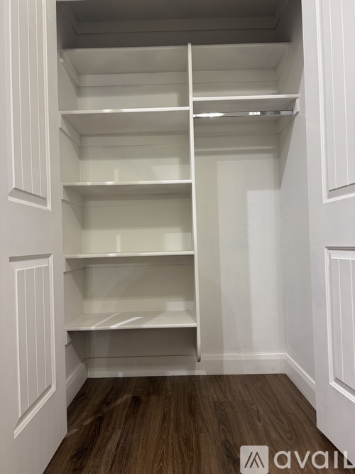 A white pantry with wood flooring and white shelves.