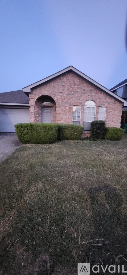 A house with a brick facade and a white door is surrounded by a grassy lawn.