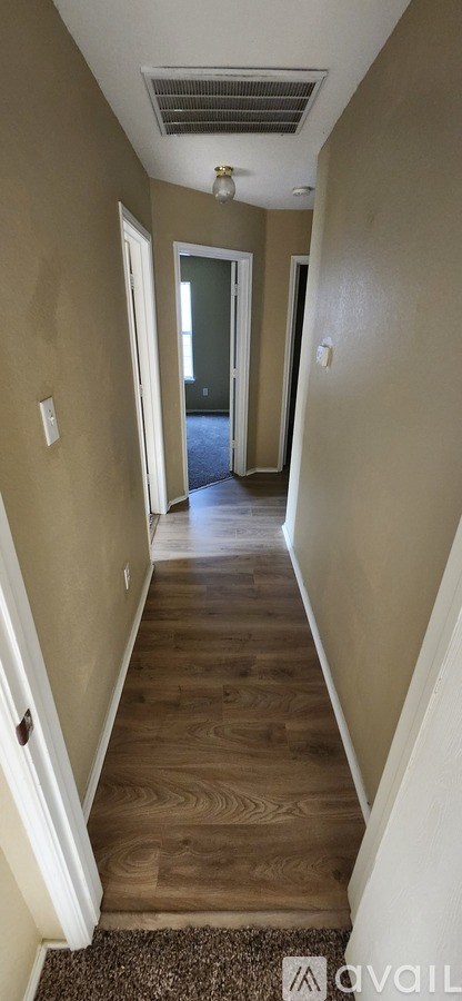 A hallway with a carpeted floor and wooden steps leading to a door.