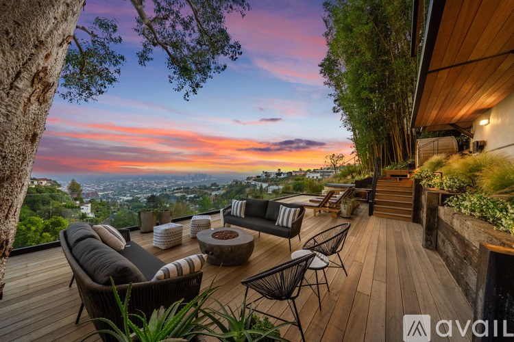 A wooden deck with a couch, chairs, and a table with a view of the city at sunset.