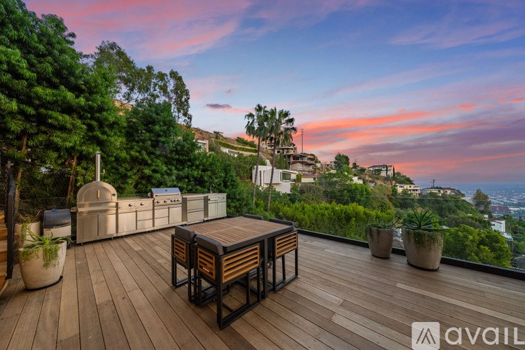 A wooden deck with a table and chairs overlooks a cityscape at sunset.