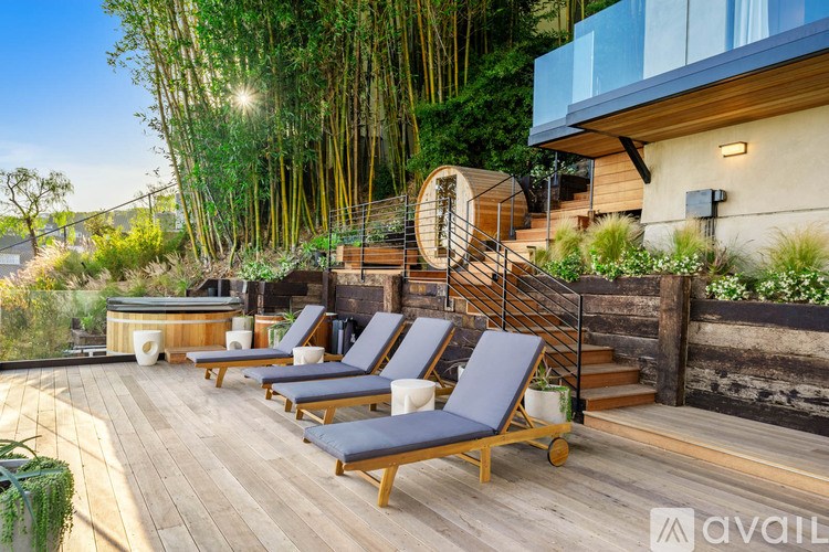 A wooden deck with lounge chairs and a hot tub surrounded by greenery.