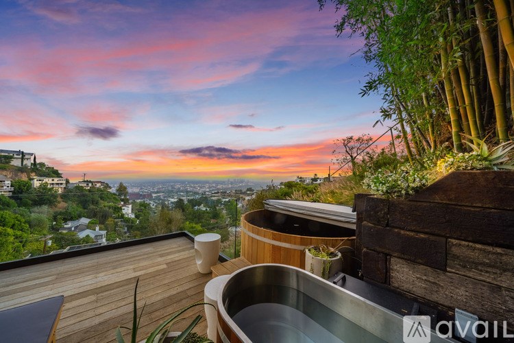 A hot tub sits on a wooden deck overlooking a cityscape at sunset.