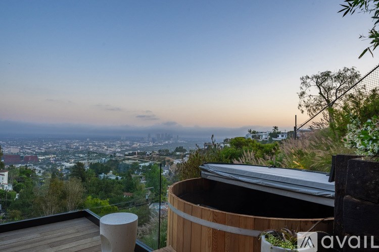 A hot tub sits on a wooden deck overlooking a cityscape at dusk.