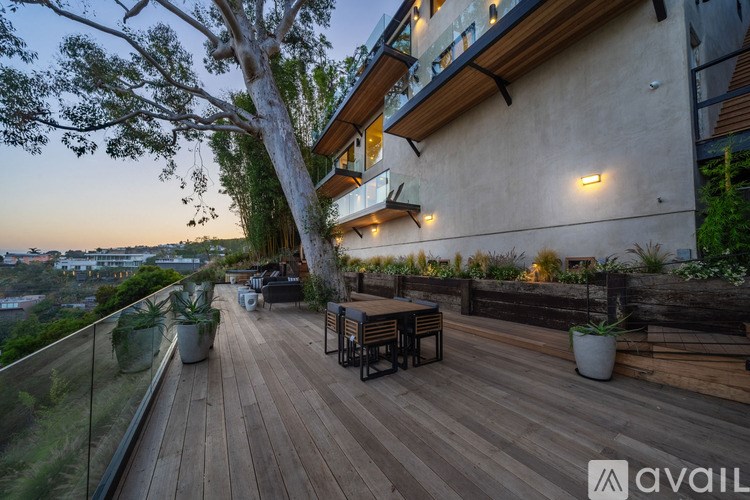 A wooden deck with a glass railing and a tree in the foreground.