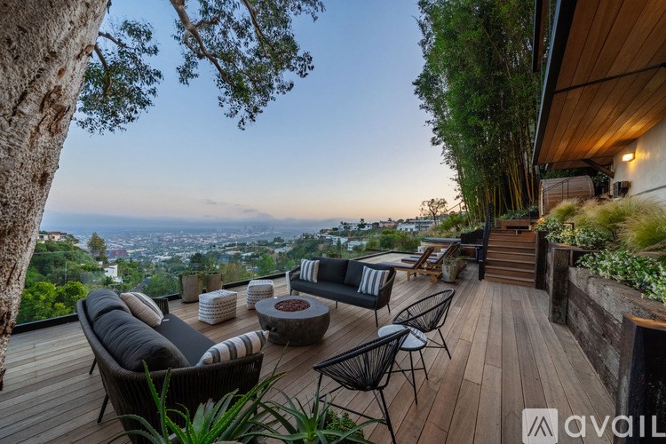 A wooden deck with a couch, chairs, and a table overlooks a cityscape at dusk.
