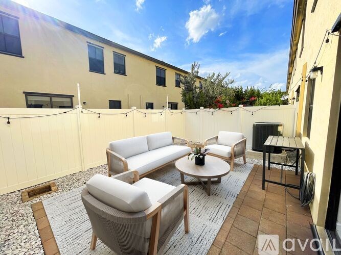 A patio with a white couch, grey armchair, and a round table with a vase of flowers on it.