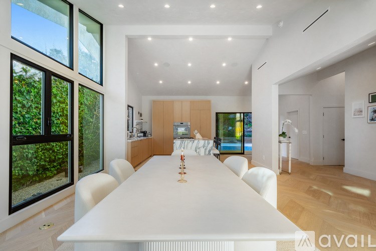 A white dining table with chairs is set up in a modern room with a large window.