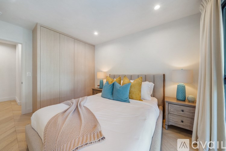 A bedroom with a large bed, a nightstand with a lamp, and a window with curtains.