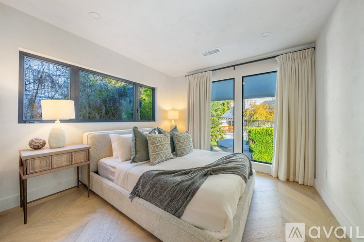 A bedroom with a large bed, a nightstand with a lamp, and a view of the outdoors through the sliding glass doors.