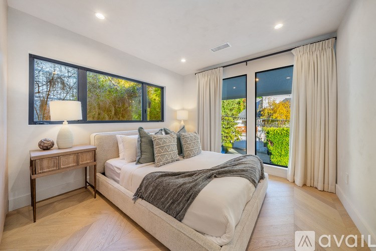 A bedroom with a large bed, a nightstand with a lamp, and a window with a view of trees.