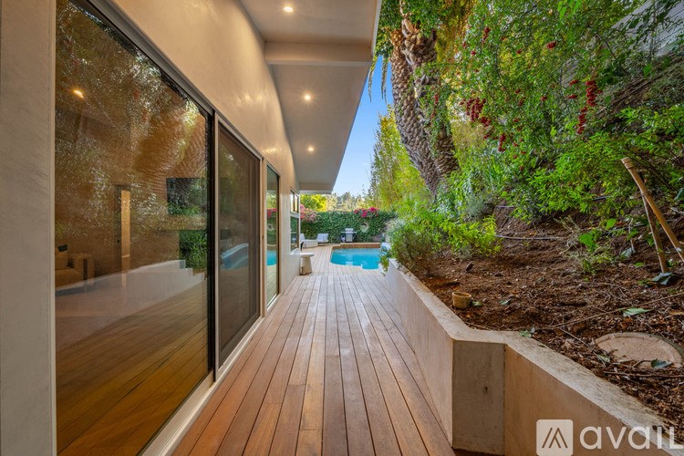 A wooden deck leads to a pool surrounded by greenery.