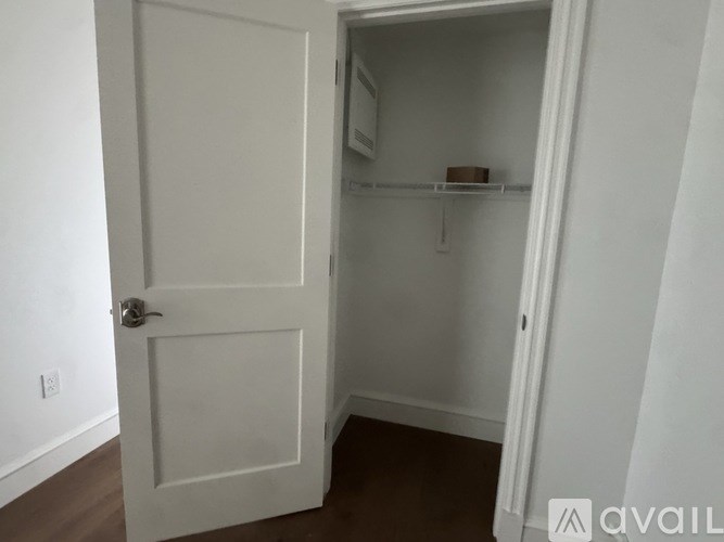 A white door is open to a small pantry with a shelf and a box on it.