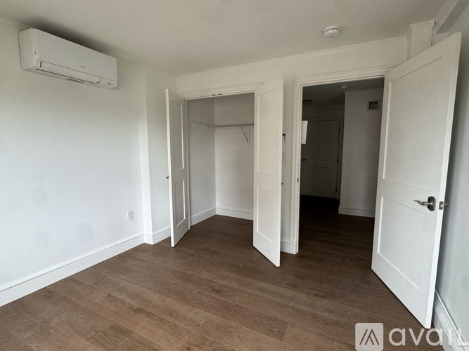 A room with a wooden floor and white walls, with a door open to another room.