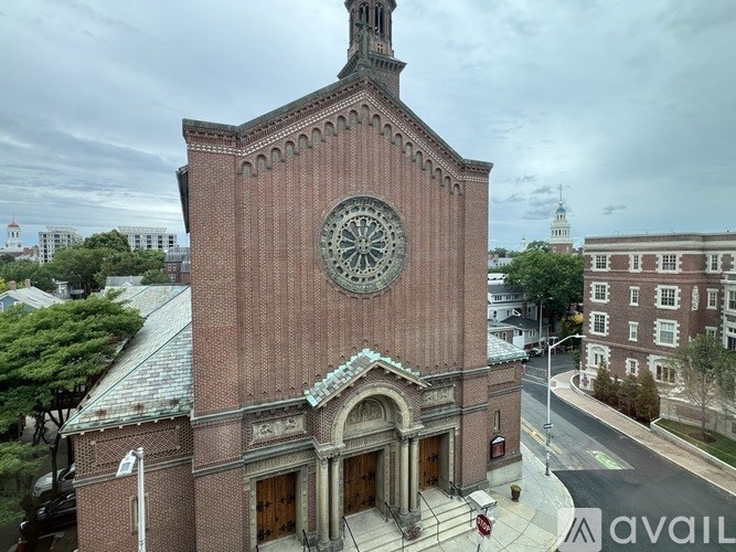 A large brick building with a clock tower is surrounded by trees and other buildings.