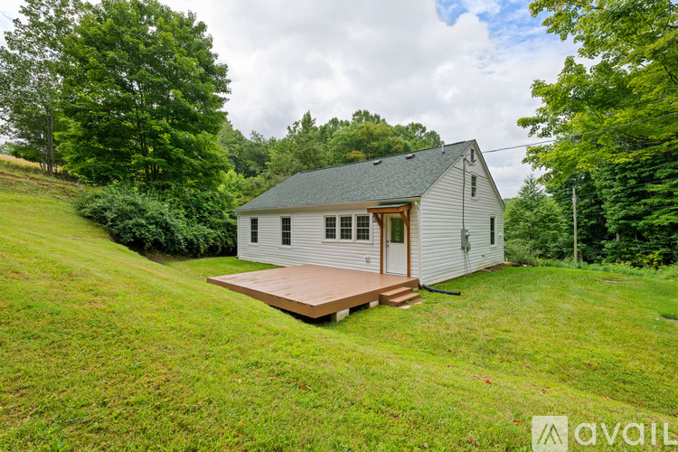 A small white house with a wooden deck in the middle of a grassy area.