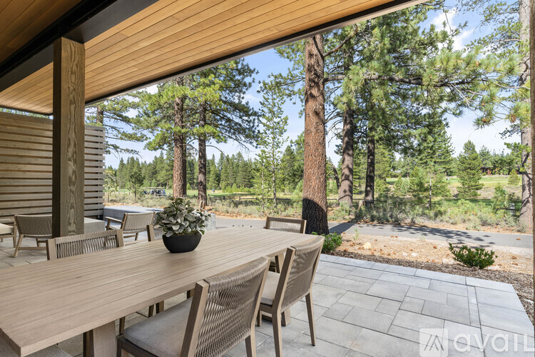 A wooden table with chairs and a potted plant on a patio with a view of trees.