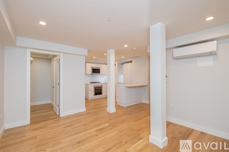 A spacious room with wooden floors and white walls, featuring a kitchen area with a refrigerator, oven, and sink.
