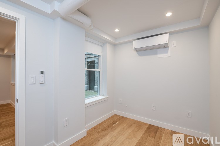 A room with a window and a white wall with a switch and a socket.