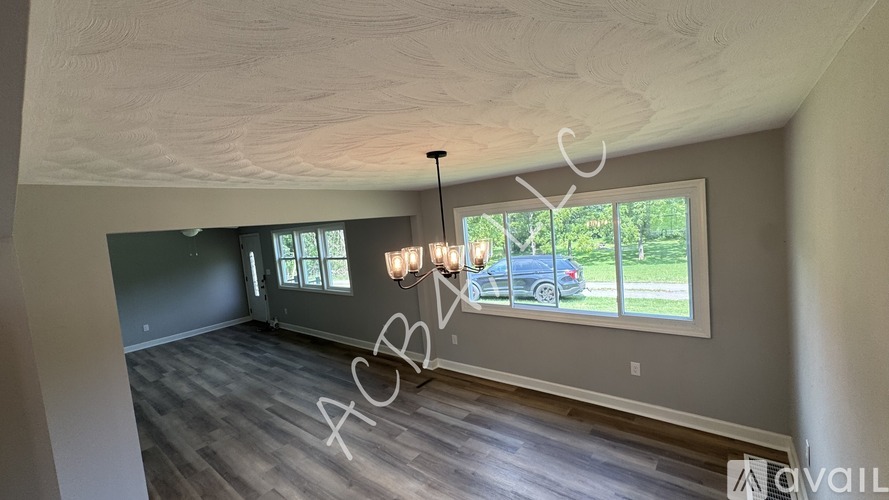 A room with wooden floors and a large window with a view of a car and trees outside.