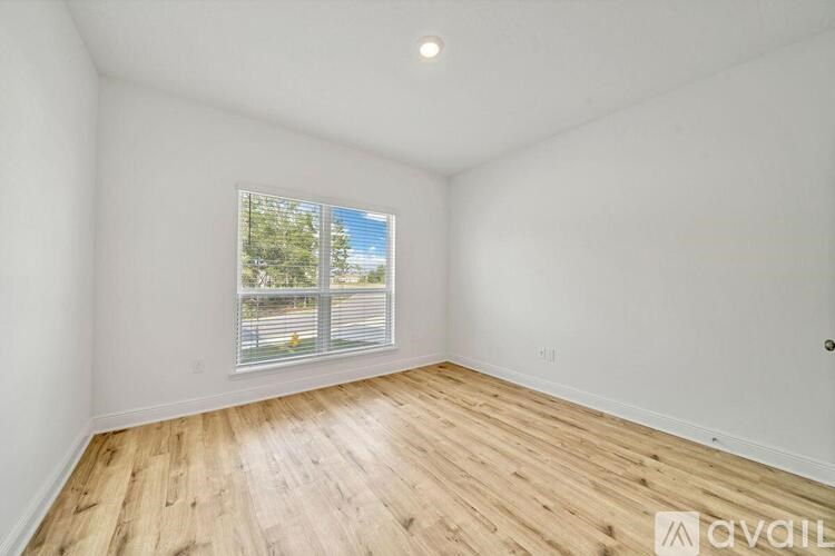 A room with wooden flooring and a window showing a view of trees and a fence.