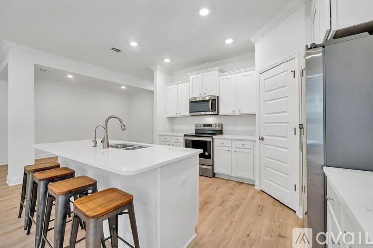 A kitchen with white cabinets and a white island with a sink and three bar stools.