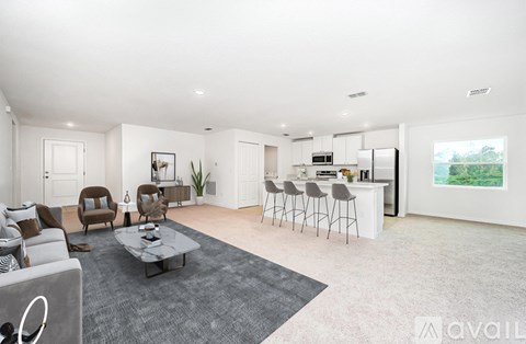 A modern living room with a grey rug and a kitchen area in the background.