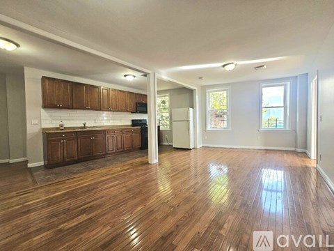 A spacious living room with hardwood floors and a kitchen area in the background.