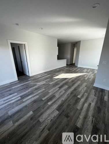 A room with wooden flooring and white walls, with a doorway leading to another room.