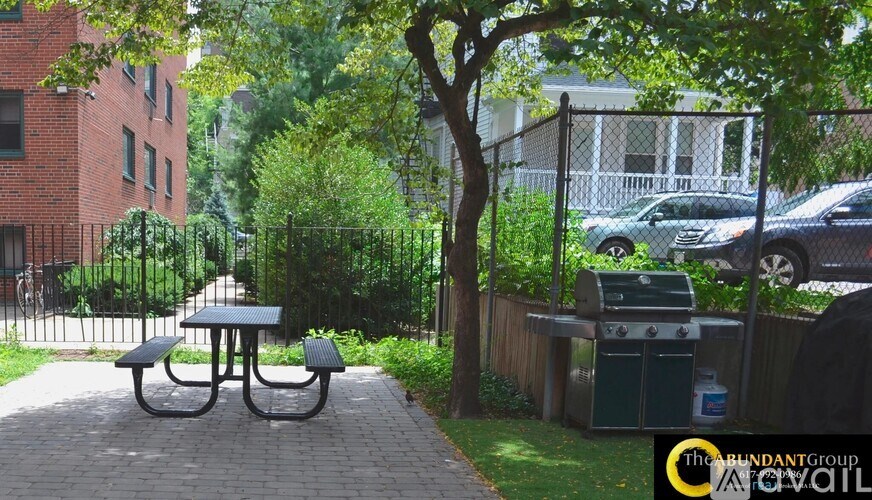 A black picnic table sits in a courtyard with a tree and a fence in the background.