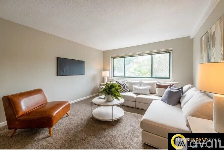 A living room with a brown leather chair, a white couch, and a flat-screen TV mounted on the wall.
