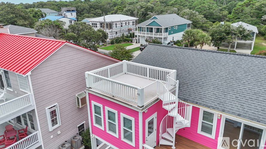 A pink house with a red roof is in the foreground of a bird's eye view of a residential area.