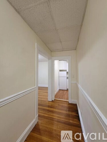 A hallway with wood floors and white walls leading to a door.