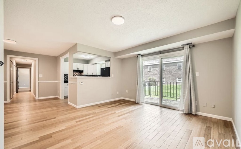 A spacious living room with wooden flooring and a sliding glass door leading to a balcony.
