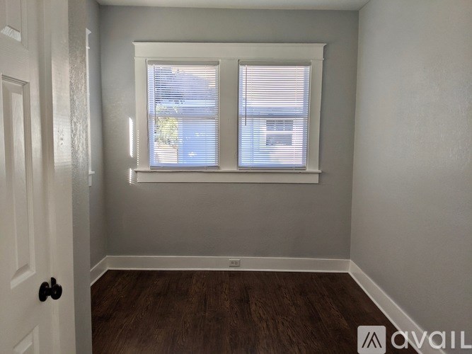 A room with a white door, a window with blinds, and a wooden floor.
