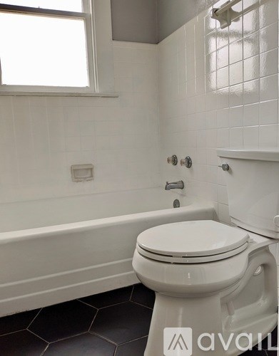 A white toilet in a bathroom with a white tub and tiled walls.