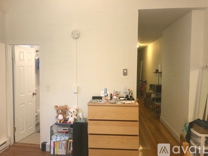 A room with a white door, a brown dresser, and a white wall with a smoke detector.
