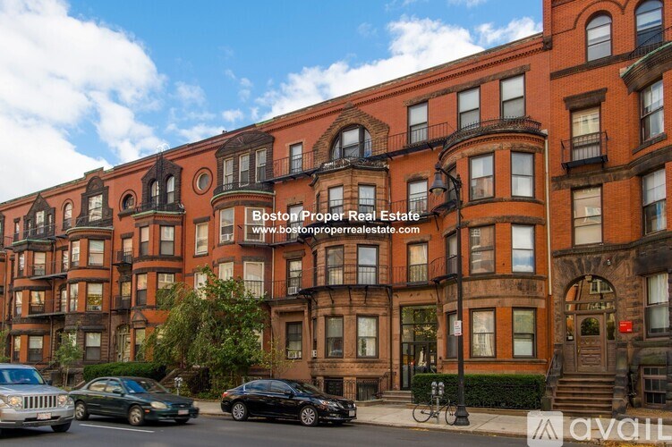 A street view of a row of brown buildings with cars parked in front and a website address for Bostonproperrealestate.com overlaid on the image.