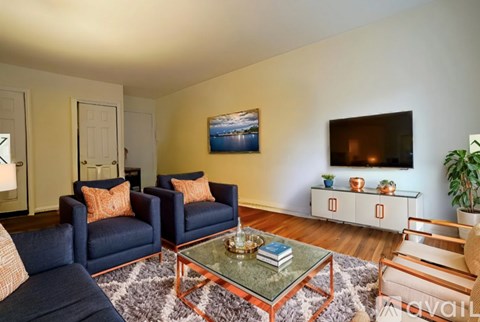 A living room with a blue couch, a glass coffee table, and a painting on the wall.