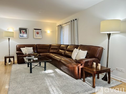 A living room with a brown leather couch and two chairs.