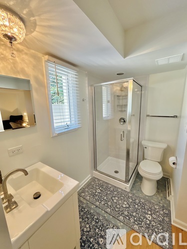 A white sink with a gold faucet is in a bathroom with a glass shower door.