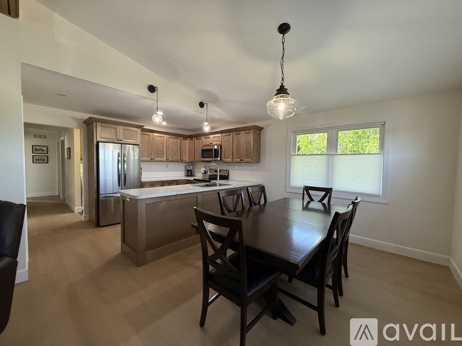 A kitchen with a table and chairs in the foreground and a refrigerator, microwave, and cabinets in the background.
