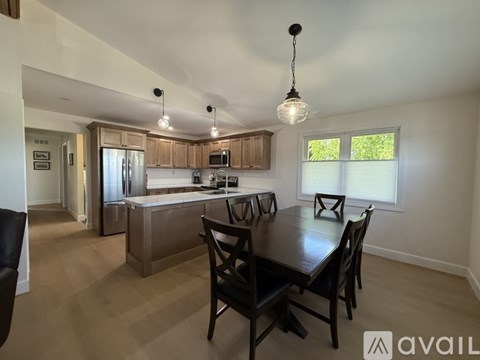 A kitchen with a table and chairs in the foreground and a refrigerator, microwave, and cabinets in the background.