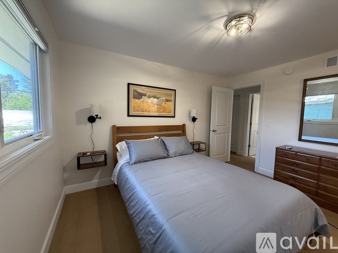 A bedroom with a bed, nightstand, and a painting on the wall.