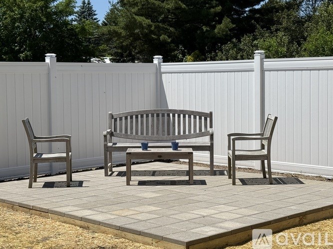 A grey bench and two chairs are placed on a patio.