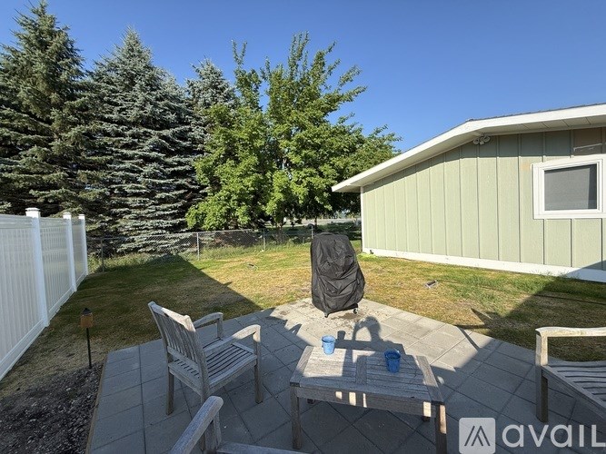 A backyard with a patio, chair, and a person covered in a black jacket.